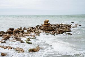zee surfen. de golven ritme tegen rotsen en stenen. een heuvel van stenen, een rotsachtig kust in de zee. de schoonheid van de zee Golf, dik schuim. foto