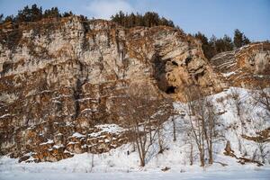 winter landschap van een rots Aan de bank van de rivier. de rotsachtig bergen van oranje kleur zijn bezaaid met sneeuw. verkoudheid Russisch winter. ural bergen foto