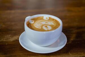 wit kop met latte staat Aan de tafel in de cafe. de origineel patroon in de kop met latte. detailopname foto