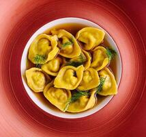 gevulde tortellini met kruiden Aan rood bord foto