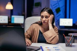 dame in zakelijke kantoor op zoek moe werken Aan laptop aan het doen na een tijdje. slim vrouw zittend Bij haar werkplaats in de Cursus van laat nacht uren aan het doen haar functie. foto