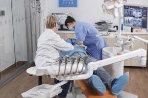 orthodontist team opereert geduldig met cariës gebruik makend van tandheelkundig gereedschap gedurende stomatologisch examen in tandheelkunde kantoor kamer. orthodontist dokter bespreken infectie behandeling met verpleegster foto