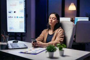 Kaukasisch ondernemer berichten in de Cursus van werken in de avond. zakenvrouw sms'en laat Bij nacht terwijl werken Aan belangrijk project gebruik makend van smartphone . foto