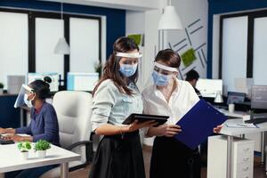 manager en werknemer stading bespreken gebruik makend van tablet pc vervelend gezicht masker. multi-etnisch bedrijf team werken met inachtneming van sociaal afstand gedurende globaal pandemisch met coronavirus. foto