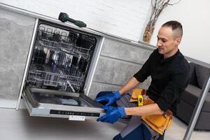 een loodgieter reparaties een vaatwasser in een keuken kamer. loodgieter Diensten. foto