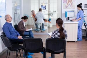 druk stomatologie aan het wachten Oppervlakte met mensen vulling het formulier voor tandheelkundig overleg. stomatoloy specialist denstiarium behandelen senior vrouw holte. receptioniste werken Aan computer. foto