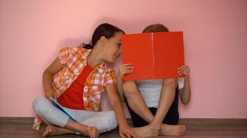 weinig meisjes lezing een boek in leven kamer. slim schoolmeisjes aan het doen hun huiswerk na school. onderwijs en afstand aan het leren voor kinderen. thuisonderwijs gedurende quarantaine. blijven Bij huis amusement. foto