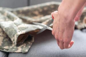 professioneel kleermaker snijdend camouflage kleding stof met schaar in werkplaats, detailopname foto