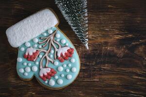 grillig vuisthandschoen vormig Kerstmis koekjes, lijsterbes boom glazuur, besneeuwd accenten, Aan een rustiek houten achtergrond. foto