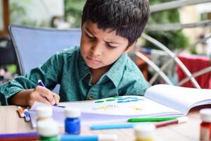 slim Indisch weinig jongen uitvoeren duim schilderij met verschillend kleurrijk water kleur uitrusting gedurende de zomer vakanties, schattig Indisch kind aan het doen kleurrijk duim schilderij tekening Aan houten tafel foto