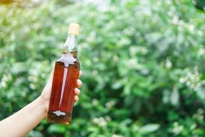 dichtbij omhoog hand- houden transparant fles welke bevat honing binnen, buitenshuis achtergrond. concept, biologisch landbouw Product van bij verhogen boerderij of natuur bronnen. foto