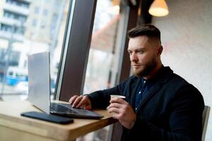 elegant zakenman aan het doen werk in mooi cafe. kop van koffie en telefoon is in de buurt hem. foto