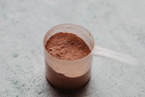schep of lepel wei-eiwit met zichtbare textuur. chocolade smaak. concrete achtergrond foto