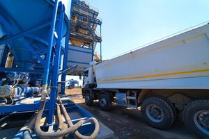 de vrachtauto is klaar naar laden grind of zand in beton station. asfalt productie, weg bouw. foto