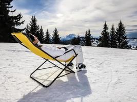 meisje zittend op de lounge stoel op sneeuw foto