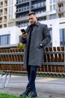 volwassen Mens in pak staand in de buurt bank met telefoon. zakenman gefocust Aan telefoon werk of functie. foto