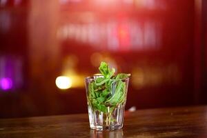 transparant glas met de bladeren van groen munt in water Aan de houten tafel. vers drinken in glas over- de wazig achtergrond. foto