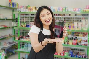 glimlachen Aziatisch vrouw net zo een Kassa is vervelend zwart schort en tonen haar telefoon scherm foto