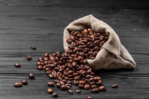 vers geroosterd koffie bonen vallend uit de zak Aan de houten oppervlak. bruin koffie bonen verspreide van zak Aan de tafel foto