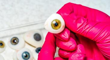 oogarts of chirurg houdt een oog, oogbol prothese in handen . concept foto voor oculair prothese, diagnose behandeling van oogheelkundig ziekten, chirurgisch operaties Aan ogen. detailopname.