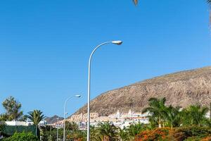 zonnig buitenwijk landschap met straat lampen en heuvel huizen onder een Doorzichtig blauw lucht in los Cristianos, tenerife. foto