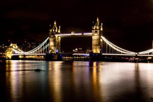 verlichte suspensie brug over- rivier- Bij nacht met reflecties Aan water. foto