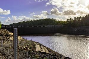 toneel- visie van een water reservoir met water niveau graadmeter, omringd door bomen onder een bewolkt lucht. foto