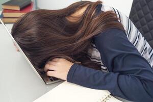 jonge vrouw lang haar valt in slaap op bureau met laptop foto