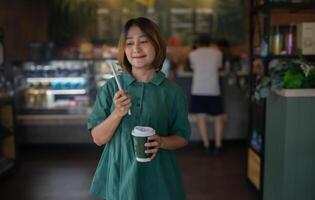 vrouw staand in de cafe Holding een drinken met een papier rietje en koffie kopje, glimlachend en op zoek Bij de camera, ontspannend Aan vakantie, levensstijl concepten. foto