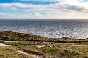 kust- landschap met met gras begroeid kliffen en Open zee onder een blauw lucht met verspreide wolken. foto