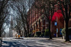 stil stedelijk straat met bomen gieten schaduwen, rood luifel Aan steen gebouw, en Doorzichtig blauw lucht in Bristol. foto