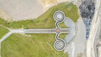 antenne visie van een kronkelend asfalt pad met loops Aan een met gras begroeid landschap, lijkt op een minimalistische ras bijhouden of een uniek tuin pad. foto