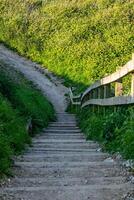 rustiek houten trappenhuis naast een aarde pad Aan een zonnig heuvel met weelderig groen in Flamborough, Engeland. foto