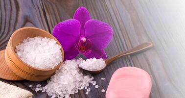 wit bad zout in een houten kom met een lepel, zeep, jute en orchidee Aan houten tafel Aan zonlicht foto