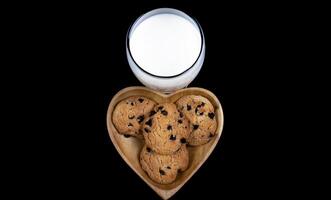 chocola spaander koekjes Aan een hart vormig bord met een glas van vers melk Aan zwart achtergrond foto