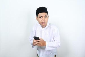 detailopname van moslim Aziatisch Mens Holding mobiel telefoon op zoek Bij camera met verward uitdrukking geïsoleerd Aan wit achtergrond foto