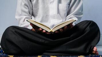 dichtbij omhoog van een moslim Mens zittend bidden en lezing de koran Aan een gebed mat. foto