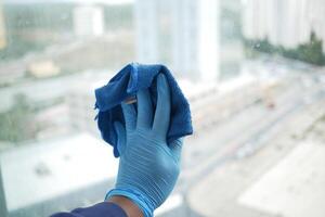 hand- in blauw handschoen schoonmaak venster met groen vod foto