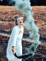 vrolijk jong vrouw met riet dansen in gekleurde rook in een veld- foto