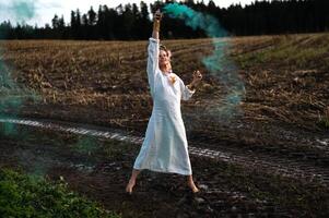 vrolijk jong vrouw met riet dansen in gekleurde rook in een veld- foto
