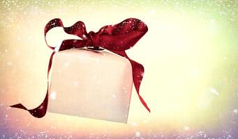 wit Kerstmis geschenk doos met een rood boog Aan een wijnoogst achtergrond met vliegend sneeuwvlokken. foto