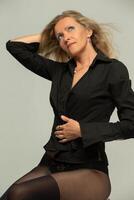 een mooi blond vrouw van over vijftig vervelend zwart kleren en kousen Aan een grijs achtergrond. foto