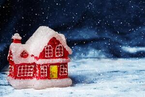een speelgoed- Kerstmis rood huis tegen de backdrop van een zwart lucht en vliegend sneeuwvlokken. foto