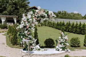 bruiloft boog gemaakt van wit bloemen en groen bladeren in de het formulier van een maan in natuur. zomer bruiloft. voorbereiding voor de bruiloft ceremonie foto