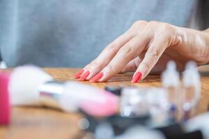 detailopname foto van een mooi vrouw hand- met rood geschilderd nagels Aan een tafel met nagel accessoires.