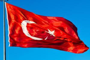 golvend Turks vlag en vlaggenmast geïsoleerd Aan blauw lucht achtergrond. nationaal vakantie van turkiye concept foto. foto