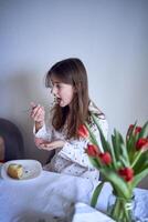 familie van drie, moeder, tiener- dochter en weinig zoon, aan het eten taart in pyjama Bij een tafel met tulpen foto
