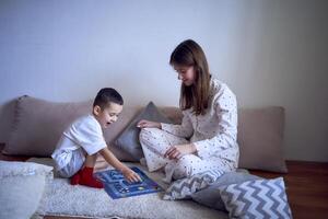 moeder met tiener- dochter en weinig zoon in pyjama spelen bord spellen Aan de verdieping foto