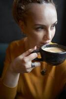 portret van een elegant middelbare leeftijd vrouw in een geel trui drinken koffie in een cafe foto