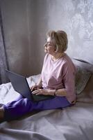 een ouderen vrouw werken met laptop Bij huis foto